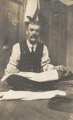 A Kirkwall tailor sits cross-legged working on a garment.